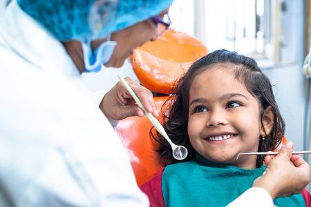 Niña en un sillón dental, sonriendo a una auxiliar de odontología