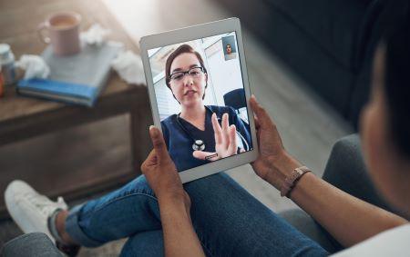 : Person holding tablet and speaking to health care professional through video.