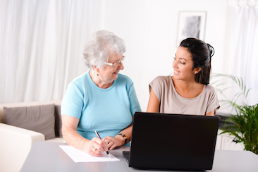 Young woman teaching older adult how to use computer