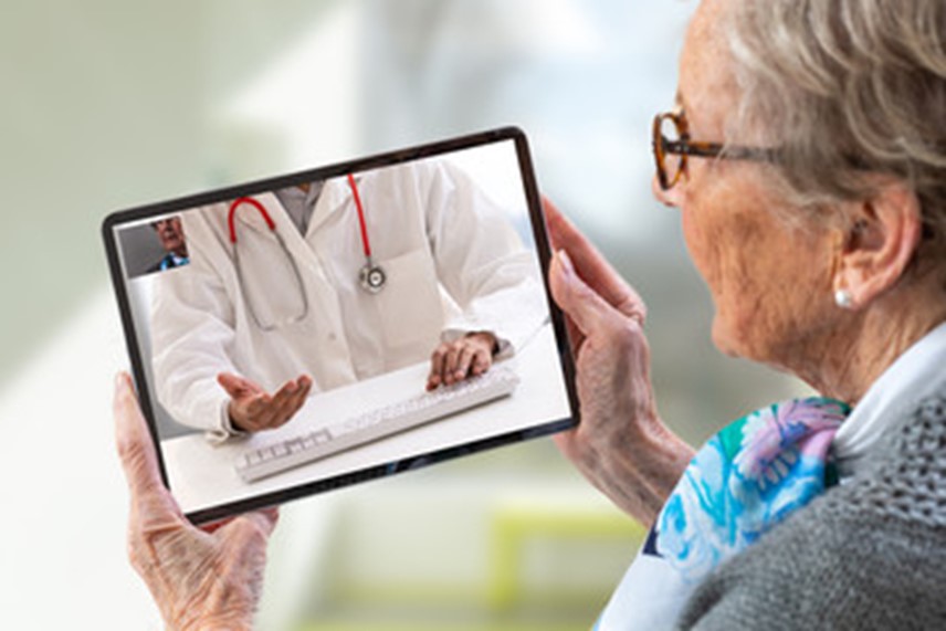 Close-up image of a pregnant woman sitting on a sofa with tablet on her lap. Health care provider appears on screen of tablet. 